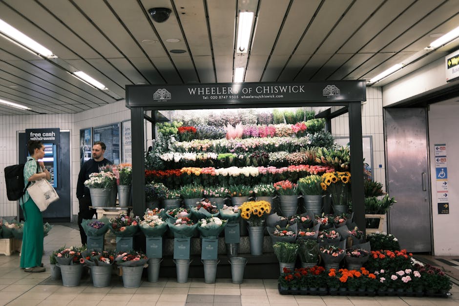 A woman with curly blonde hair selecting a bouquet of mixed fresh flowers at a florist shop, which includes pale pink roses, bright yellow daisies, and white chrysanthemums arranged in tall, clear gla