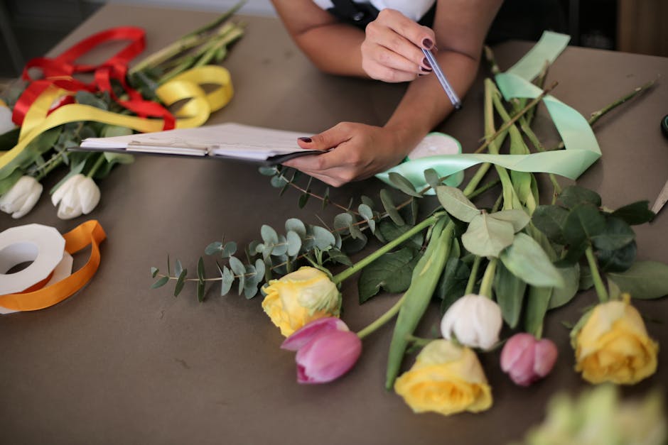 A floral delivery scene inside a florist shop with dark green wooden walls and a glass display case filled with various colourful flower arrangements in the background. One woman with curly blonde hai